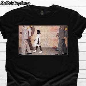 Könnte beinhalten: Schwarzes T-Shirt mit einem gerahmten Bild eines jungen Mädchens in einem weißen Kleid, das von Erwachsenen in Anzügen begleitet wird. Das Bild zeigt eine historische Szene mit Fokus auf Bürgerrechte und soziale Gerechtigkeit. Das Shirt hat den Text "Ms Printing Lady" oben.