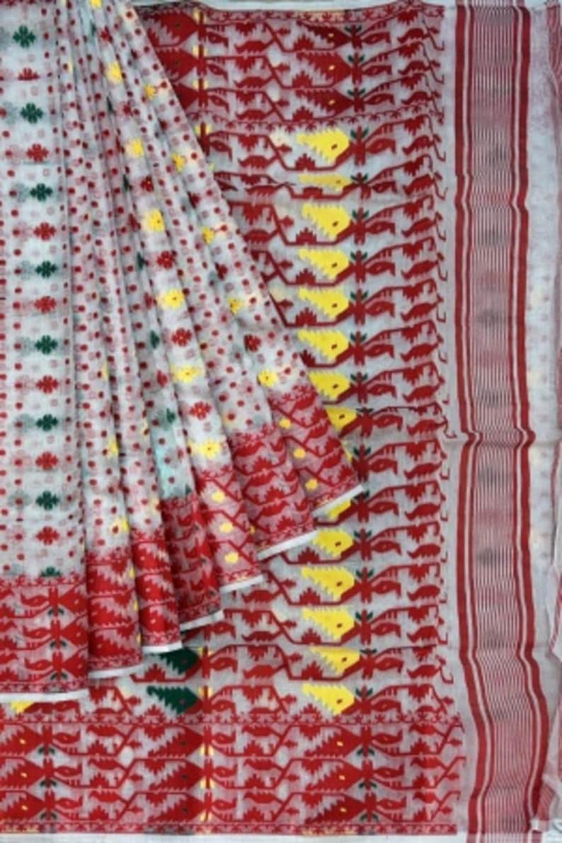 May include: White saree with red, yellow, and green geometric patterns. The saree has a white base with a red border and a repeating pattern of red, yellow, and green geometric shapes.