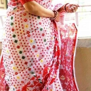 May include: A white and red saree with a polka dot pattern and floral designs. The saree has a red border with white stripes.