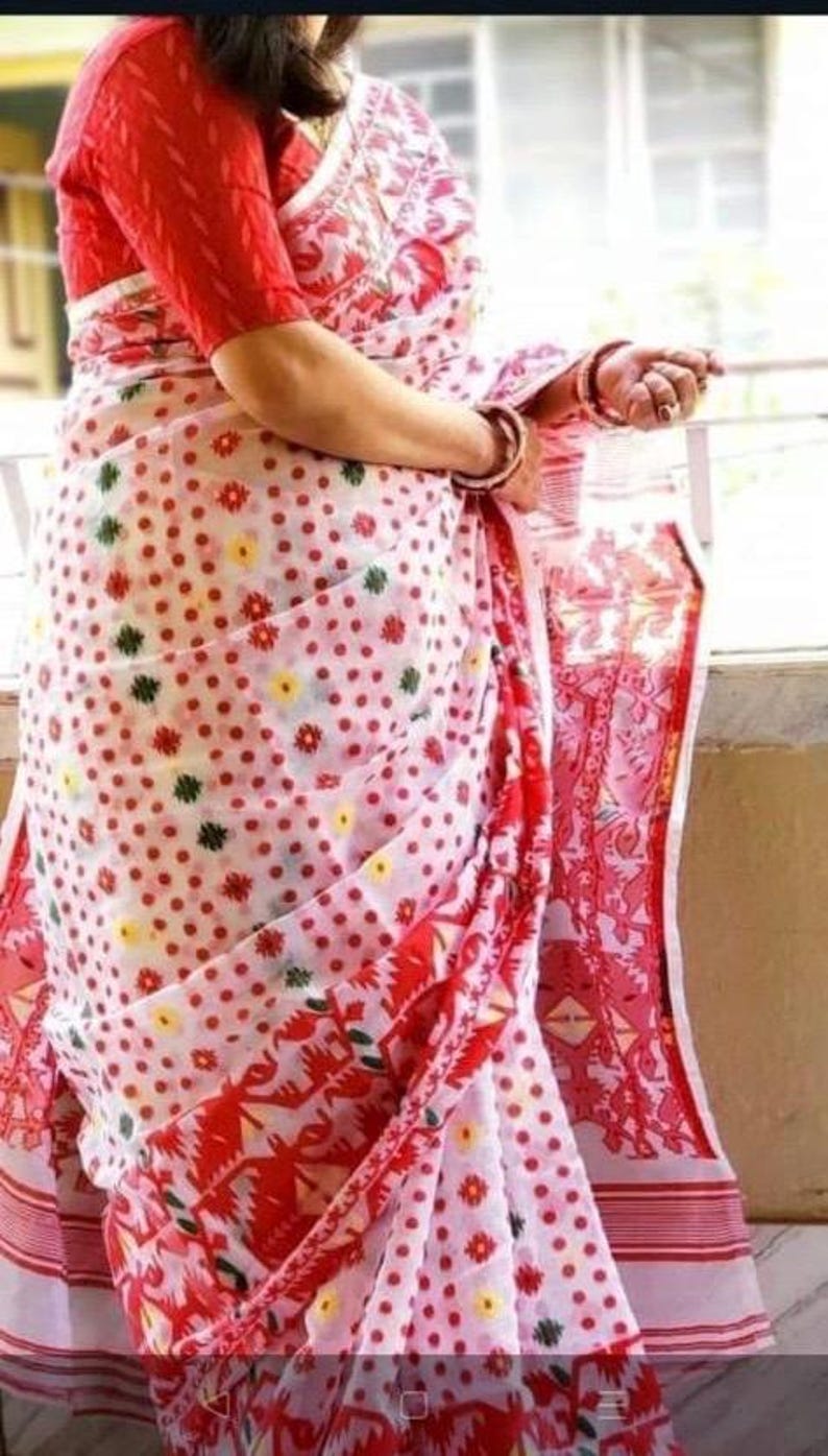 May include: A white and red saree with a polka dot pattern and floral designs. The saree has a red border with white stripes.