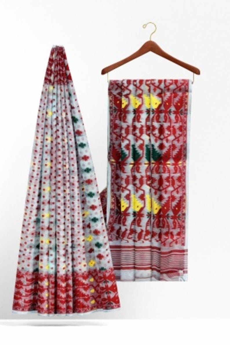 May include: A white and red patterned saree with yellow and green accents. The saree is draped over a hanger.