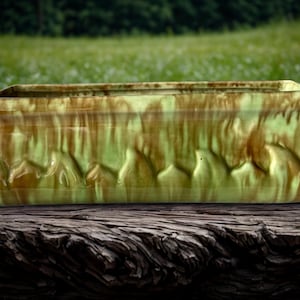 May include: A rectangular ceramic planter with a textured, glazed finish. The planter has a light green base with brown accents and a wave-like pattern. It sits on a weathered wooden surface. The planter is suitable for plants.