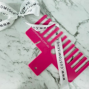 May include: Pink plastic tool with a comb on one side and a hole in the centre. The tool is labelled "www.customisehq.com.au" and "customisehq.com.au".