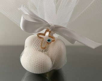 May include: White tulle favor bag with a white satin ribbon tied around it. A gold cross charm with a blue evil eye is attached to the ribbon.