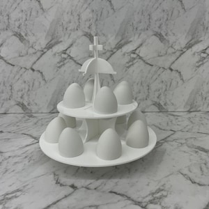 May include: White egg holder with a tiered design. The holder is made of plastic and has a cross-shaped top. It can hold up to 10 eggs.