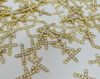 May include: A large group of gold-toned cross charms with clear rhinestones. The charms have a loop at the top for attaching to jewelry.