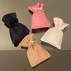 K&ouml;nnte beinhalten: Vier kleine Stoffbeutel mit Kordelzug in verschiedenen Farben: Schwarz, Rosa, Wei&szlig; und Beige. Die Beutel sind aus strukturiertem Stoff und haben ein schlichtes Design.