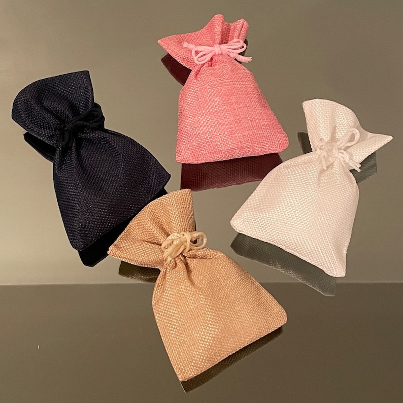 K&ouml;nnte beinhalten: Vier kleine Stoffbeutel mit Kordelzug in verschiedenen Farben: Schwarz, Rosa, Wei&szlig; und Beige. Die Beutel sind aus strukturiertem Stoff und haben ein schlichtes Design.