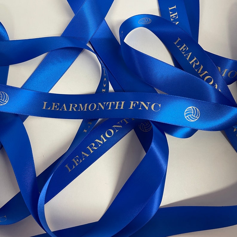 May include: Blue satin ribbon with the text "LEARMONTH FNC" and a volleyball graphic printed in gold.
