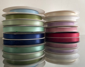 May include: A stack of spools of satin ribbon in various colors, including light blue, green, white, purple, pink, red, navy blue, and lavender. The spools are arranged in two stacks, one on the left and one on the right.