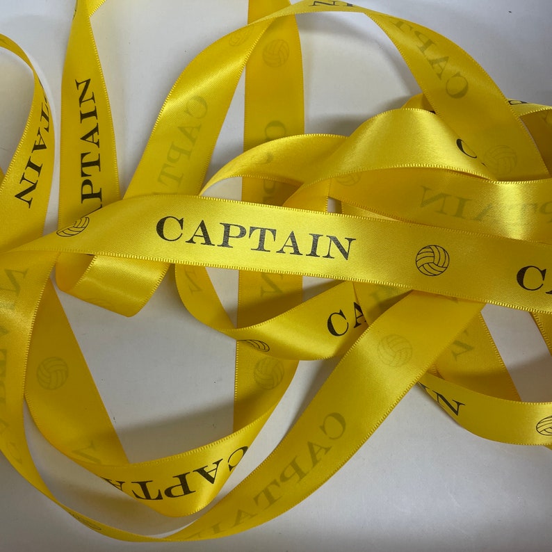 May include: Yellow satin ribbon with the word "CAPTAIN" printed on it. The ribbon is decorated with small volleyball images.