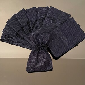 K&ouml;nnte beinhalten: Ein Set mit 12 kleinen, dunkelblauen Jutes&auml;ckchen mit Kordelzug. Die S&auml;ckchen sind f&auml;cherf&ouml;rmig angeordnet, wobei das oberste S&auml;ckchen umgeklappt ist, um den Kordelzug zu zeigen.