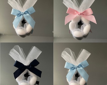 May include: Four white tulle favor bags with different colored satin bows. The bags are filled with white almond-shaped candies. The bows are blue, pink, black, and light blue.