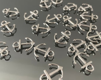 May include: A collection of silver-toned metal anchor charms. The anchors are scattered on a reflective surface.