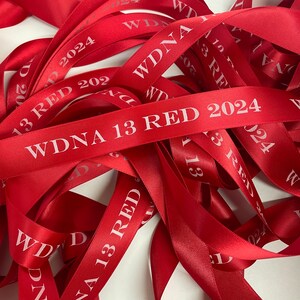May include: A pile of red satin ribbons with the text "WDNA 13 RED 2024" printed on them.