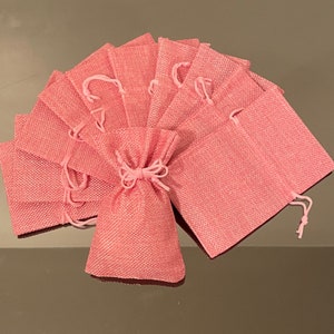 K&ouml;nnte beinhalten: Eine Gruppe von rosa Jutes&auml;cken mit Kordelzug. Die S&auml;cke sind f&auml;cherf&ouml;rmig angeordnet, wobei die &Ouml;ffnungen der S&auml;cke nach au&szlig;en zeigen.