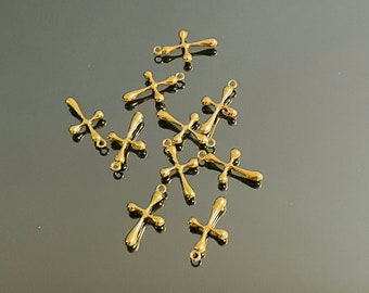 May include: A collection of gold-colored cross charms. Each cross has a rounded, smooth design with a small loop at the top for attaching to jewelry. The crosses are scattered on a reflective surface.