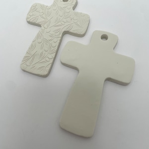May include: Two white ceramic cross ornaments. One cross features a raised design of leaves and berries. The other cross is plain.