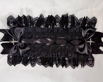 May include: A black lace headband with satin bows and decorative cross accents. The headband features intricate lace detailing and is designed with a gothic aesthetic. The bows are positioned on either side of the headband.