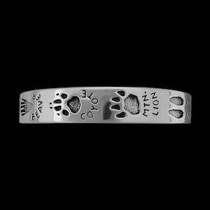 May include: Silver bracelet with animal paw prints and the words "BEAVER", "COYOTE", "MTN. LION" engraved around the band.
