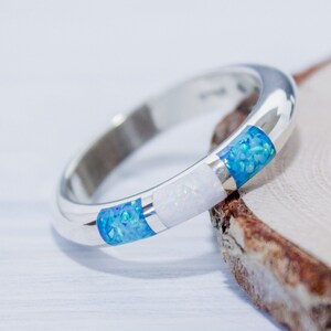 May include: A silver band ring with three inlaid gemstones. The ring features a white opal stone in the center, flanked by two blue opal stones.