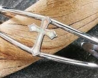 May include: A silver bangle bracelet with a cross-shaped design featuring a white iridescent inlay. The cross is set within a double-band design.