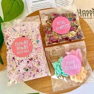 May include: A selection of small, clear plastic bags containing colourful confetti, flower-shaped soaps, and pink fizzy dust. The bags have pink circular labels with text like "Flower Power" and "Petal Confetti".