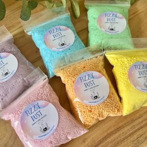 May include: Several small, clear plastic bags filled with brightly coloured granular powder. Each bag has a circular label with the text "Fizzy Dust" and "Simply Add Water!" in various colours, such as pink, blue, and yellow.
