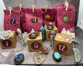 May include: An advent calendar with burgundy paper bags, each numbered and clipped with wooden clothespins. The calendar includes various crystals, gemstones, and a bracelet. The bags are decorated with white snowflakes and stickers.
