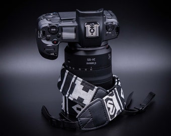 May include: A black Canon camera with a 24-105 lens attached, sitting on a black and white camera strap.