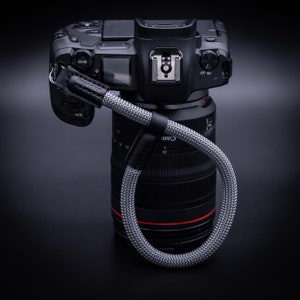 May include: A black camera with a lens attached and a gray camera strap with the word "Inception" printed on it.