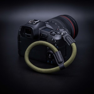 May include: A black camera with a green and black camera strap. The camera has a lens cap on the lens.