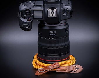 Op de afbeelding: Een zwarte Canon EOS camera met een 24-105 mm lens. De camera ligt op een gele en bruine cameraband.