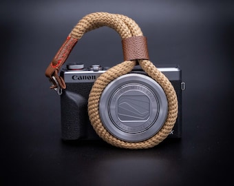 Op de afbeelding: Een zilveren Canon camera met een bruine touwen camera-riem. De camera lens heeft de tekst "Canon Zoom Lens 4.2x 15 8.8-36 mm 1:1.8-2.8".