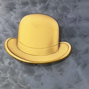 May include: A gold-colored bowler hat pin with a rounded crown and a curved brim. The hat has a band around the crown and is set against a textured, gray background. The pin is a classic accessory.