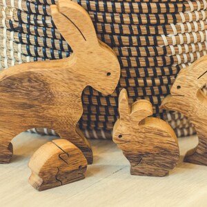 Pu&ograve; includere: Quattro statuine di coniglio in legno, intagliate in un colore marrone chiaro, sono disposte su una superficie in legno chiaro. I conigli sono tutti di dimensioni diverse e hanno pose diverse. Il coniglio pi&ugrave; grande &egrave; in piedi con le orecchie dritte. Gli altri tre conigli sono seduti con le orecchie basse.