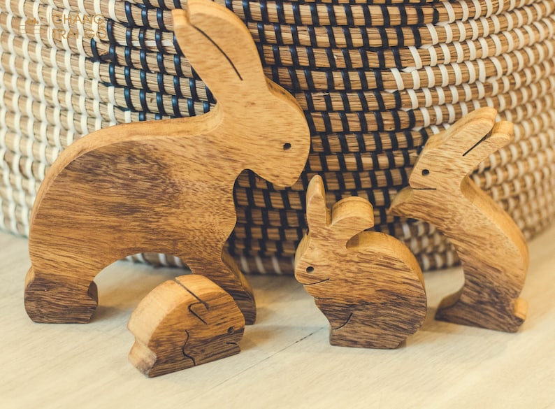 Pu&ograve; includere: Quattro statuine di coniglio in legno, intagliate in un colore marrone chiaro, sono disposte su una superficie in legno chiaro. I conigli sono tutti di dimensioni diverse e hanno pose diverse. Il coniglio pi&ugrave; grande &egrave; in piedi con le orecchie dritte. Gli altri tre conigli sono seduti con le orecchie basse.