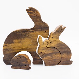 Pu&ograve; includere: Un set di tre figurine di coniglio in legno, intagliate in un colore marrone scuro con una venatura del legno. I conigli sono disposti in un gruppo familiare, con il coniglio pi&ugrave; grande dietro e il coniglio pi&ugrave; piccolo davanti.