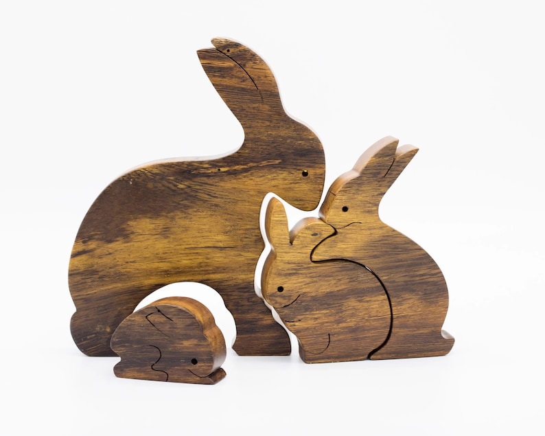 Pu&ograve; includere: Un set di tre figurine di coniglio in legno, intagliate in un colore marrone scuro con una venatura del legno. I conigli sono disposti in un gruppo familiare, con il coniglio pi&ugrave; grande dietro e il coniglio pi&ugrave; piccolo davanti.