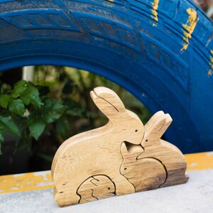 Pu&ograve; includere: Un puzzle di legno di una famiglia di conigli con tre pezzi. La madre coniglio &egrave; il pezzo pi&ugrave; grande, seguita dal padre coniglio e poi dal bambino coniglio. I pezzi sono fatti di legno naturale e hanno un colore marrone chiaro.
