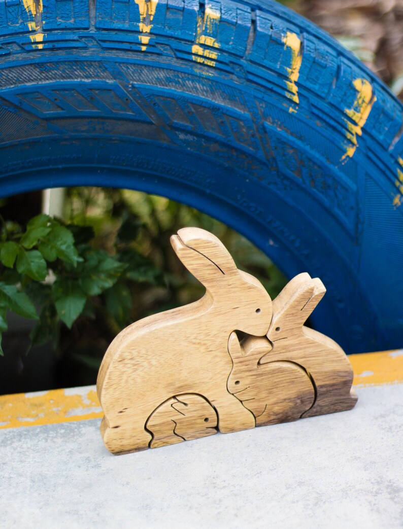 Pu&ograve; includere: Un puzzle di legno di una famiglia di conigli con tre pezzi. La madre coniglio &egrave; il pezzo pi&ugrave; grande, seguita dal padre coniglio e poi dal bambino coniglio. I pezzi sono fatti di legno naturale e hanno un colore marrone chiaro.