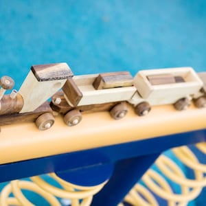 May include: A wooden toy train set with a locomotive and three cars. The train is made of natural wood and has a brown and natural wood finish. The train is on a yellow track.