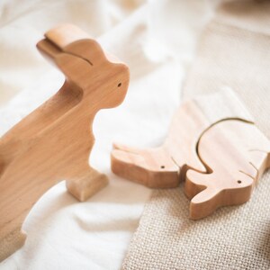Pu&ograve; includere: Tre pezzi di puzzle di animali in legno, un coniglio, un rinoceronte e un pesce, sono disposti su una superficie di tessuto marrone chiaro. I pezzi sono in legno marrone chiaro e hanno una finitura liscia.