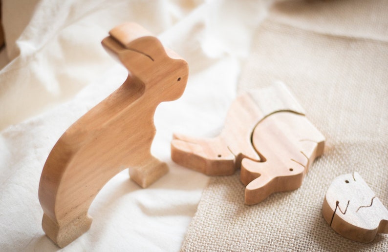 Pu&ograve; includere: Tre pezzi di puzzle di animali in legno, un coniglio, un rinoceronte e un pesce, sono disposti su una superficie di tessuto marrone chiaro. I pezzi sono in legno marrone chiaro e hanno una finitura liscia.
