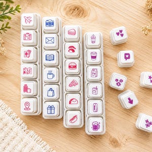 May include: A collection of white square rubber stamps featuring various icons in pink and blue ink. The stamps are arranged in four vertical strips and several individual pieces, displaying symbols for travel, food, drinks, hearts, and stars.