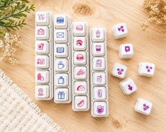 May include: A collection of white square rubber stamps featuring various icons in pink and blue ink. The stamps are arranged in four vertical strips and several individual pieces, displaying symbols for travel, food, drinks, hearts, and stars.