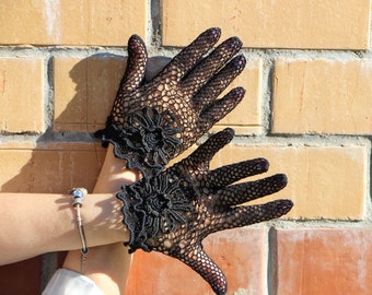 May include: A pair of black lace gloves with floral detailing. The gloves are made of a delicate, crocheted fabric and have a vintage look.