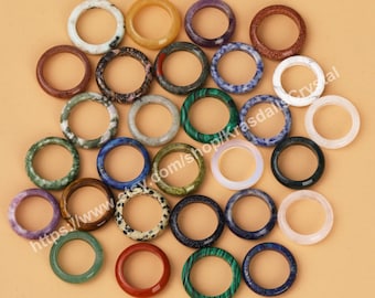 Può includere: Una collezione di 25 anelli in pietre preziose colorate. Gli anelli sono realizzati con diverse pietre naturali, tra cui ametista, agata, diaspro e occhio di tigre. Gli anelli sono tutti di dimensioni e forme diverse, ma hanno tutti una larghezza di circa 1,25 cm. Gli anelli sono disposti in cerchio su uno sfondo marrone chiaro. https://www.etsy.com/shop/KrasdallaCrystal