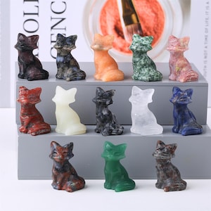 Puede incluir: Una colección de pequeñas figuras de zorro talladas en varios colores y materiales. Los zorros están sentados y parecen estar hechos de piedra o cristal. Los colores incluyen rojo, verde, naranja y azul.