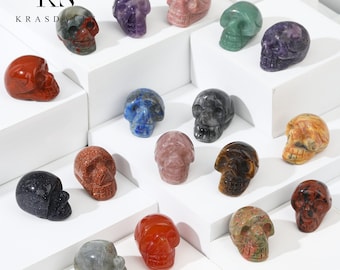 May include: A collection of 17 small, hand-carved crystal skull figurines in various colors, including red, blue, green, purple, and brown. The skulls are displayed on white surfaces.
